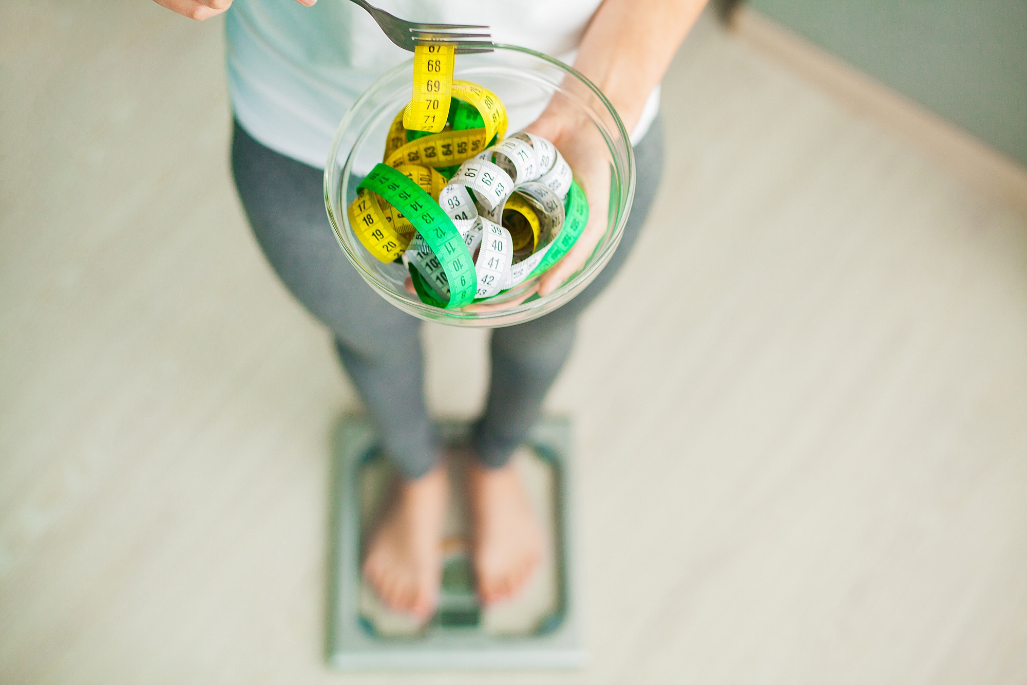 Diet and Weight Loss. Woman holds bowl and fork with measuring tape